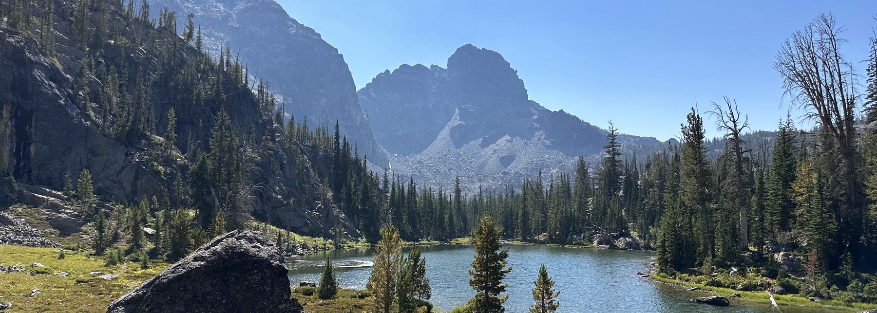 An alpine lake beneath a granite Sawtooth peak, ringed by conifers