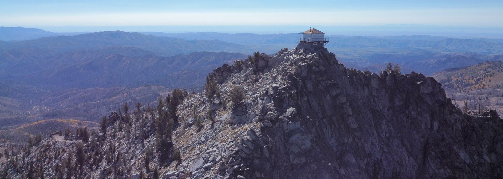 A fire lookout on a rocky summit above forested Idaho ridges